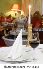 glass with wine, white napkin and candle at table, fountain in restaurant