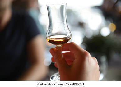 A Glass With Wiskey In Hand Of Man With Blurred Background. Concept Of Whiskey Tasting.