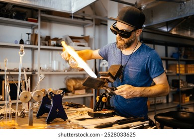 A glassblowing male artisan carefully heats and shapes molten glass with a torch to create a vase in his workshop. - Powered by Shutterstock