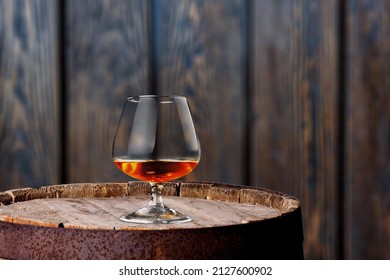 Glasses Of Alcohol Stand On Barrels Of Cognac In Wine Cellar Illuminated By Soft Light