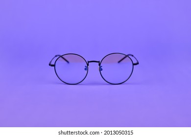 Glasses With A Blue Light Filter To Protect The Eyes While Working At The Computer. Round Glasses For Filtering Blue Light. Stylish Round Eyeglasses On A Purple Background, Top View.