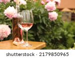 Glasses and bottle with rose wine on wooden table near beautiful peonies, space for text