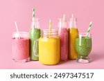 Glasses and bottles of different tasty smoothie with straws on pink background