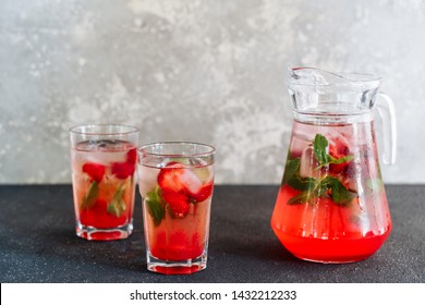 Glasses and Carafe with Fresh Strawberry Lemonade. Cold Refreshing Mixed Berries with Herbal Mint and Ice Beverage Cocktail in Cup and Decanter. Summer Juicy Vitamin Drink Side View