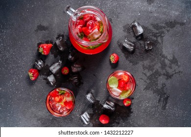 Glasses And Carafe With Strawberry Soda Drink. Cool Refreshing Homemade Lemonade Mixed Ripe Berries And Herbal Mint. Splash Of Water And Ice Around Of Cup Isolated On Black Background. Top View