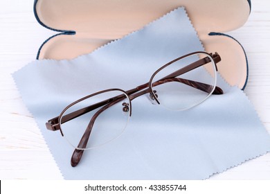 Glasses and case with glasses cleaning cloth on white wooden table 
