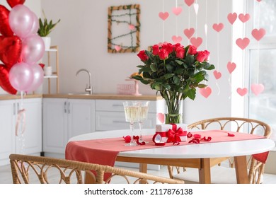 Glasses of champagne, engagement ring, flowers and gift box on dining table in kitchen