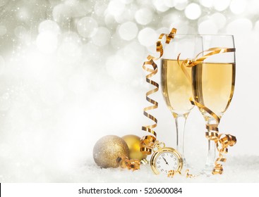 Glasses with champagne and golden Christmas balls against holiday lights - New Year background