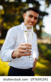 Glasses With Champagne In The Hand Of Beautiful Young Man. Stylish Groomsman Or Best Man Of Groom Congratulates And Says Toast. Elegant Man Holding Glasses Of Champagne At Luxury Wedding. Celebration