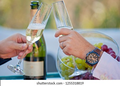 Glasses Of Champagne In Hand. Male Strong Hands, A Gay Couple Celebrates Their Wedding. Holiday, Party, Alcohol.hand With A Clock And A Glass.  