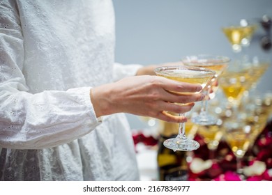 Glasses Of Champagne In The Hands Of A Waitress Girl, Light Sparkling Wine, Distribution Of Glasses With Whiskey, Cocktail Party, Alcoholic Beverages Spill. High Quality Photo