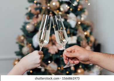 Glasses of champagne on the background of Christmas tree lights. New Year eve. Feast of Christmas. Loving couple banging champagne glasses on New Year's night