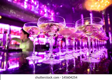 Glasses of champagne on bar counter with barman professional, which making cocktail drinks in background, soft focus - Shutterstock ID 145604254