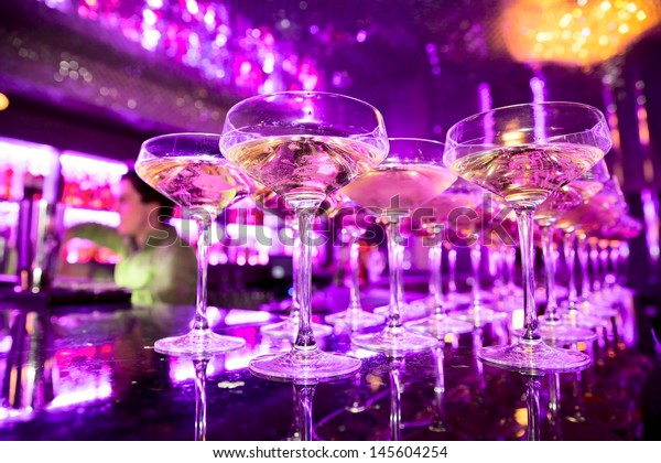 Glasses of\
champagne on bar counter with barman professional, which making\
cocktail drinks in background, soft\
focus