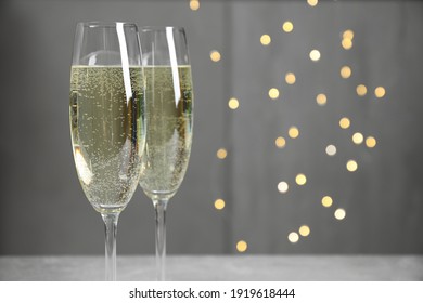 Glasses of champagne on light grey background with blurred lights. Space for text