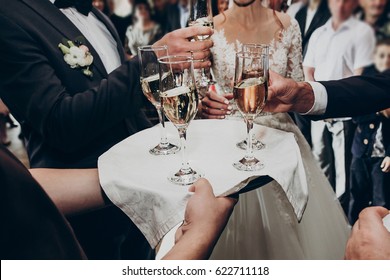 glasses of champagne on tray, hands holding glasses and toasting, celebrating wedding. stylish happy newlyweds with family cheering. space for text. luxury wedding reception