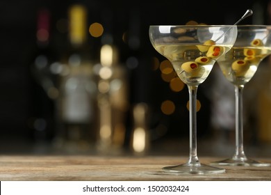 Glasses of Classic Dry Martini with olives on wooden table against blurred background. Space for text