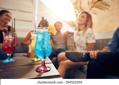 Glasses Of Cocktail On Table With Young People Sitting On Sofa On Roof Top. Friends Having A Rooftop Party.