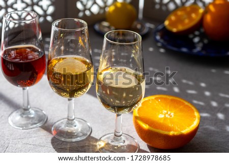 Glasses with cold dry fino and sweet cream sherry fortified wine and orange in summer sunlights, andalusian style interior on background