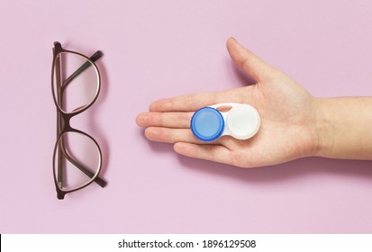 Glasses and contact lens case in human hand on purple background. Concept of choice the way vision correction. Flatly, copy space
