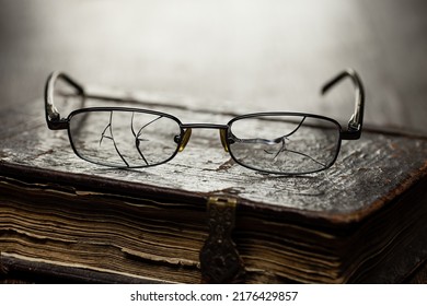 Glasses With Cracked Glasses On An Antique Book In A Leather Antique Binding, Studio Shot.