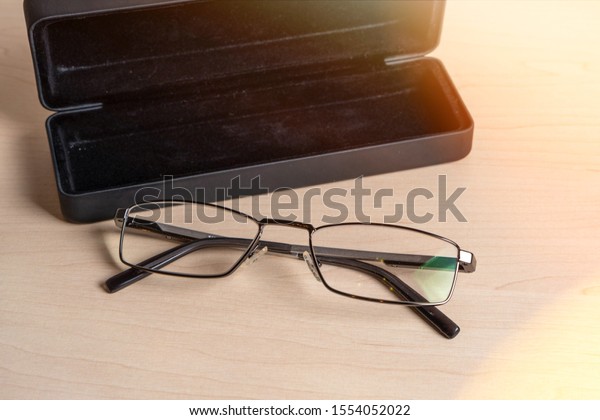 Glasses and a dark blue case on a light wooden\
table. Eyeglass storage and\
care