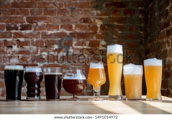 Glasses of dark and light beer and ale in\
sunlight on brick wall background. Cold delicious alcohol drinks\
are prepared for a big friend\'s party. Concept of holiday, fun,\
meeting, oktoberfest.