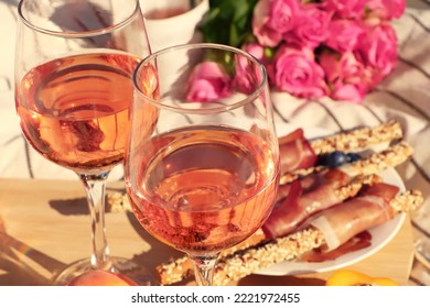 Glasses Of Delicious Rose Wine, Flowers And Food On White Picnic Blanket, Closeup