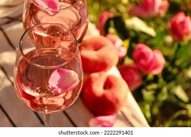 Glasses Of Delicious Rose Wine With Petals On White Picnic Blanket Outside. Space For Text