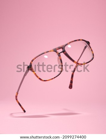 Glasses float in air touching pink surface. Minimal retro-stlyle.