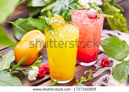 Glasses with fresh lemonade in summer greenery and flowers on the background of a wooden table, citrus and berry lemonade with frappe ice on a wooden table top on the background of a summer garden