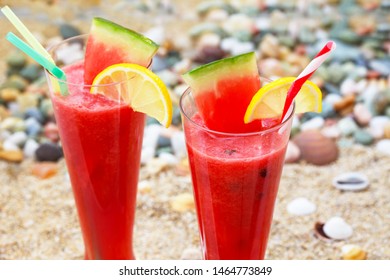 Glasses with fresh watermelon juices on sandy beach. Healthy summer refreshment on vacation. Red cocktail with watermelon and lemon.