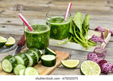Glasses with freshly squeezed organic juices from vegetables and fruits on a wooden background with cut lime, cucumber and spinach. Detox diet. Next to it lies a centimeter