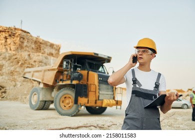 In glasses and hard hat. Worker in professional uniform is on the borrow pit at daytime.