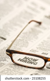 Glasses Highlighting A NOW HIRING Classified Ad In A Newspaper.