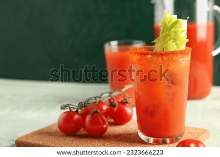Glasses and jug of bloody mary with celery on green wooden table