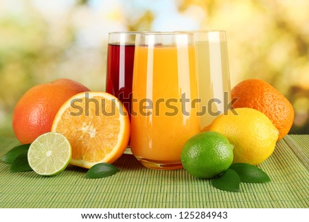Glasses of juise with leafs and fruits on table on bright background
