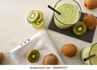 Glasses With Kiwi Drink On Slate Plate On White Wooden Bench Full Of Fruits With White Napkin. Top View.