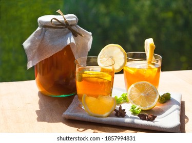 Glasses with kombucha, lemons and mint, a jar with a fermented drink stand on a wooden table against the backdrop of green trees. Healthy food concept.