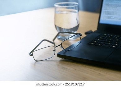 Glasses leaning against a dark black laptop with code on a wooden desk with a glass of water in an office, business concept in cold light, copy space, selected focus, narrow depth of field - Powered by Shutterstock