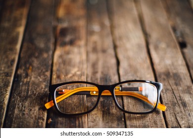  glasses  lie on the dark wooden table.   Black orange  glasses on wooden table. Office workplace with glasses on wood table. Glasses with orange rim. Orange Case for storage points.