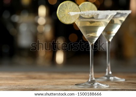 Glasses of Lime Drop Martini cocktail on wooden table against blurred background. Space for text