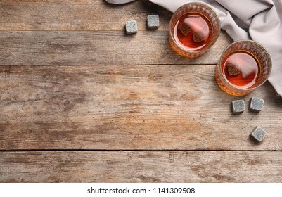 Glasses with liquor and whiskey stones on wooden background, top view