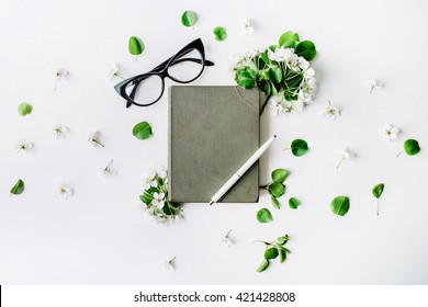 Glasses, old book, pen and branches with leaves and flowers on white background. Flat lay composition