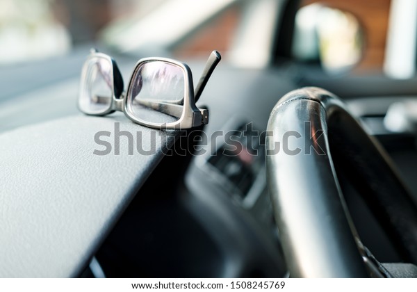 Glasses are on the dashboard of the\
car, next to the steering wheel, on a blurred\
background.