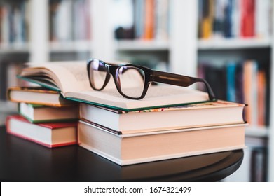 Glasses on stack of books. Library in the background. Books and glasses.
