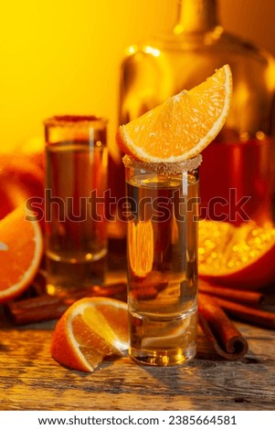 Glasses of orange liqueur garnished with sugar and cinnamon powder. Orange liqueur with fresh fruits on an old wooden table.