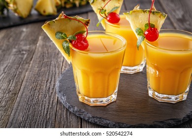 Glasses Of Pineapple Juice With Pieces Of Pineapple, Cocktail Cherry  And Mint On Wooden Table, Healthy Drink Concept.