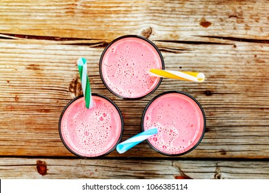 Glasses of pink strawberry smoothies, milkshake or cocktail isolated on wooden background. From top view