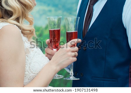 Glasses with red champagne drink in bride and groom hands. Happy newlyweds drinking. Loving couple created new family.